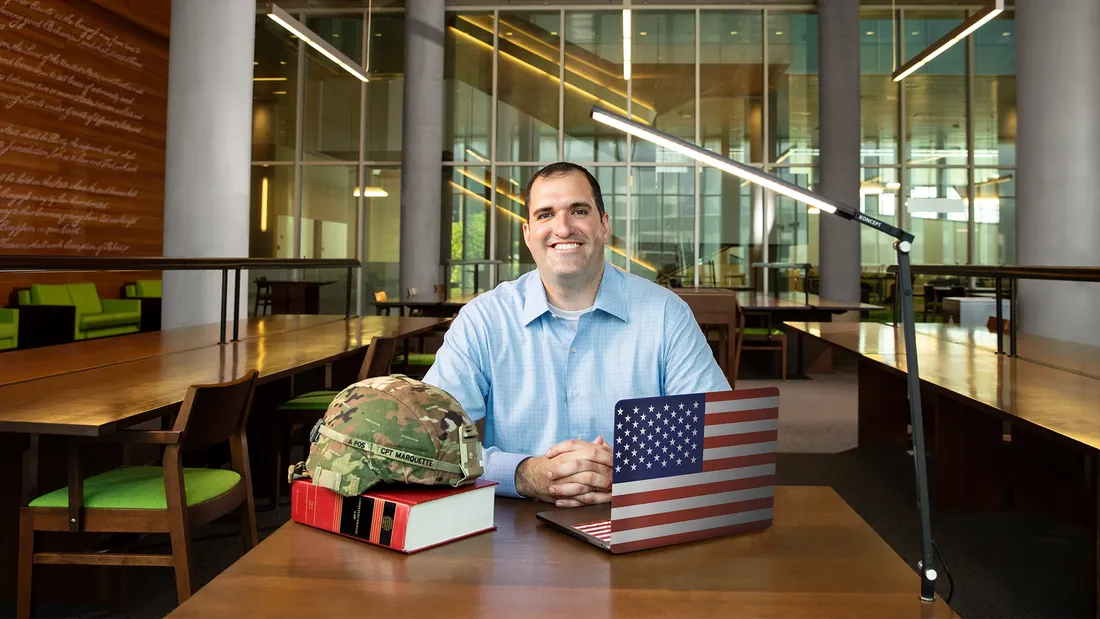 Ryan Marquette sitting at a desk smiling.