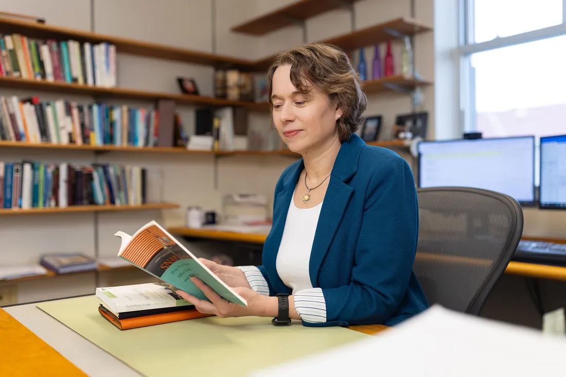 A professor sitting at a table reading and smiling.