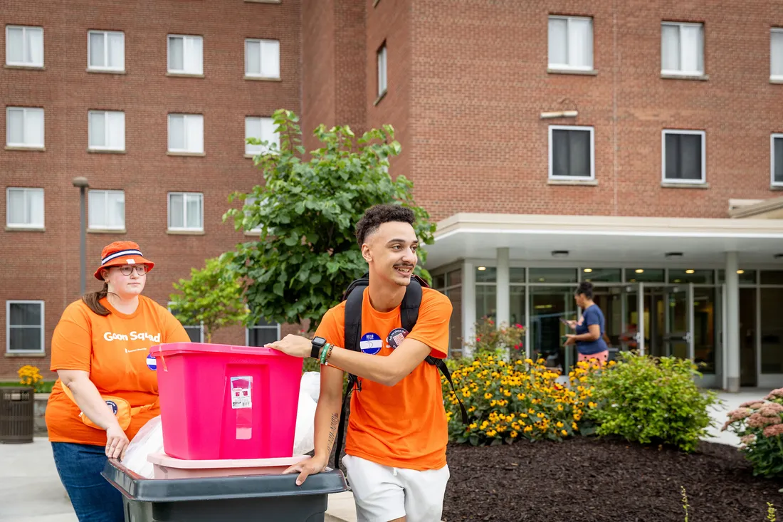 Student worker pushing a cart while walking alongside another person.