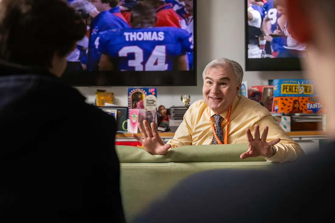 Person sitting on couch talking to room of people.