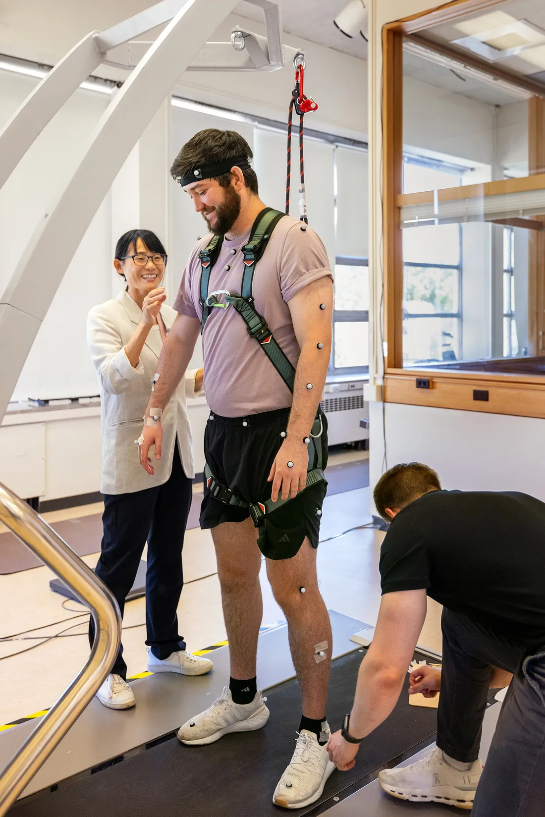 Person walking on a treadmill while two other people run lab tests on her.