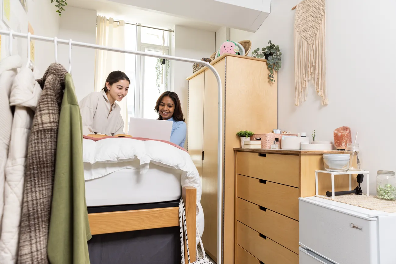 Two students look at a computer in their dorm room together.