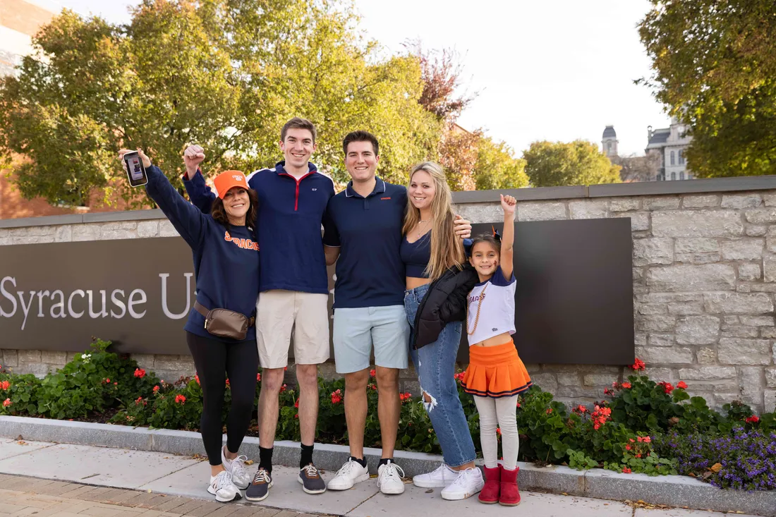 A family stands together in front of the Syracuse University sign during family weekend.