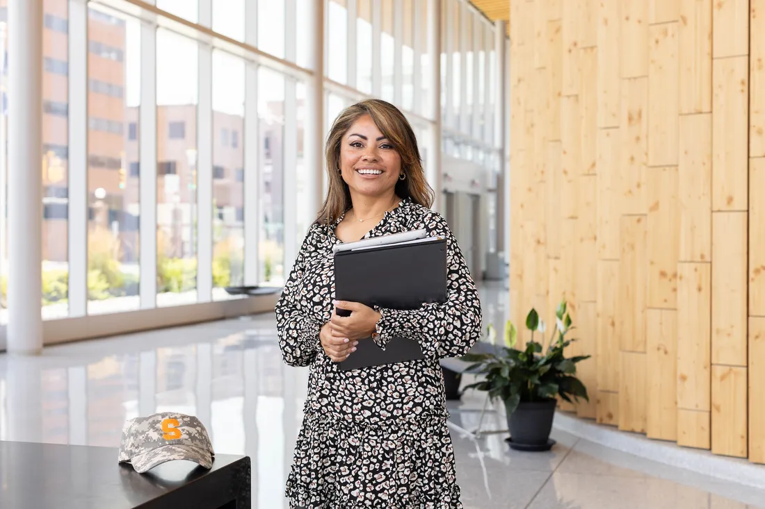 Person holding books while standing and smiling.