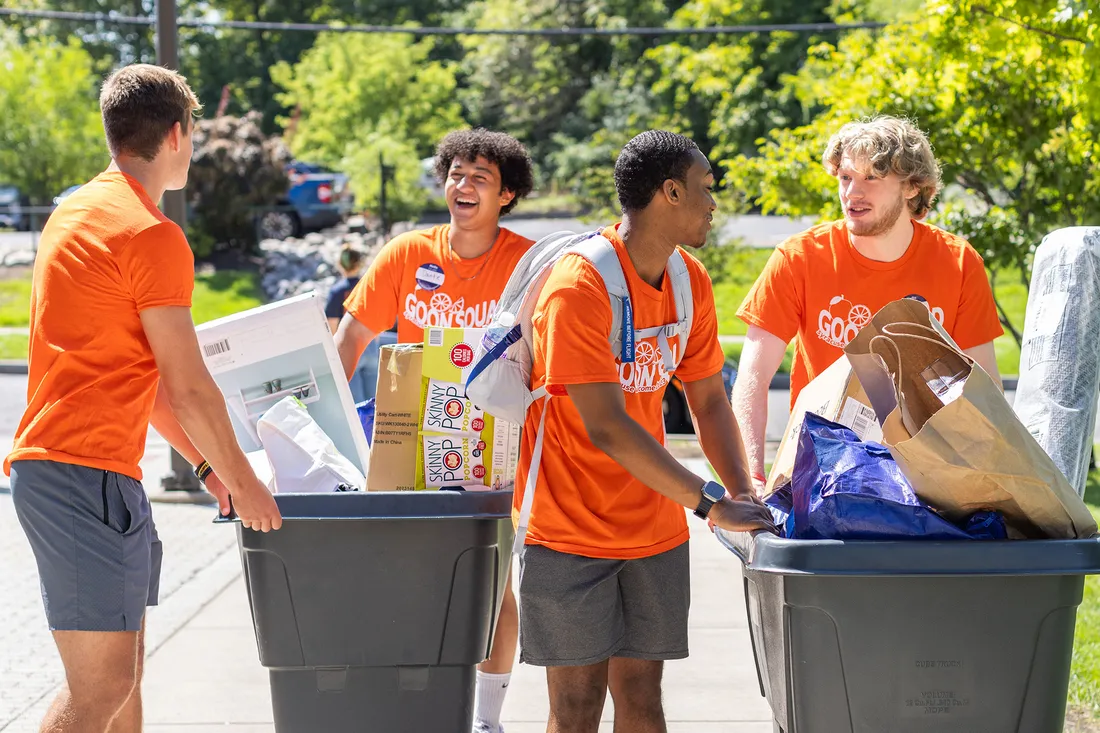 Students in orange tee shirts help new students move into dorms.