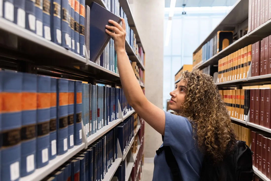 A student taking a book off the shelf at the library.