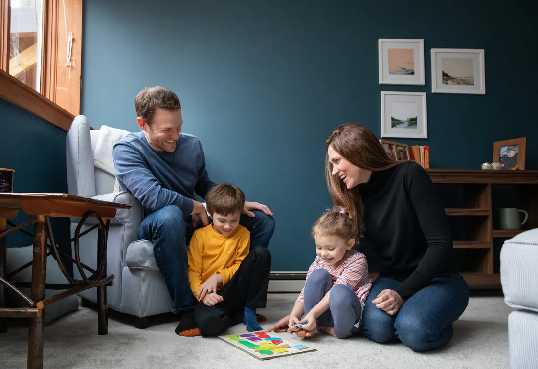 Two adults and two children sitting in a room playing a game on the floor.