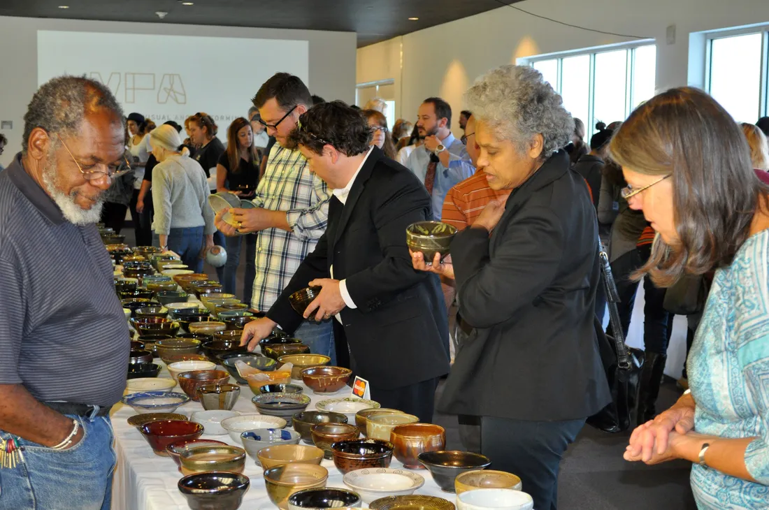 People standing in front of a long table with numerous ceramic bowls