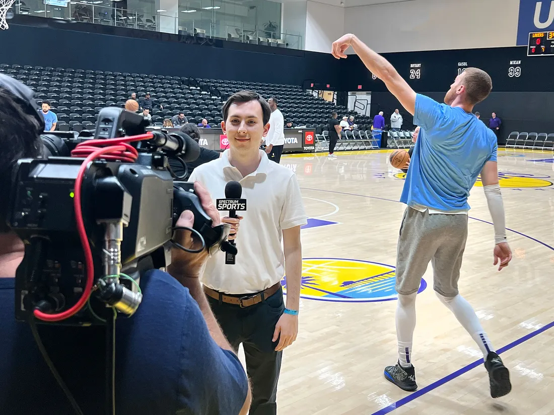 Luke Backman sideline reporting at a basketball game inside of a gym.