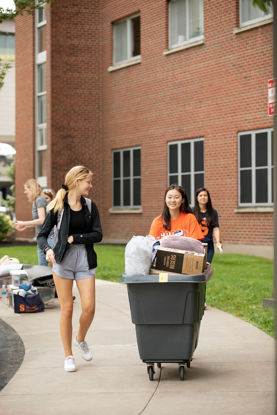 Student worker pushing a cart while walking alongside another person.