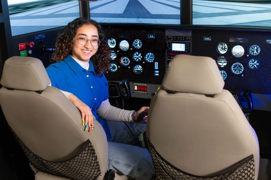A student sitting at a control panel while smiling at the camera