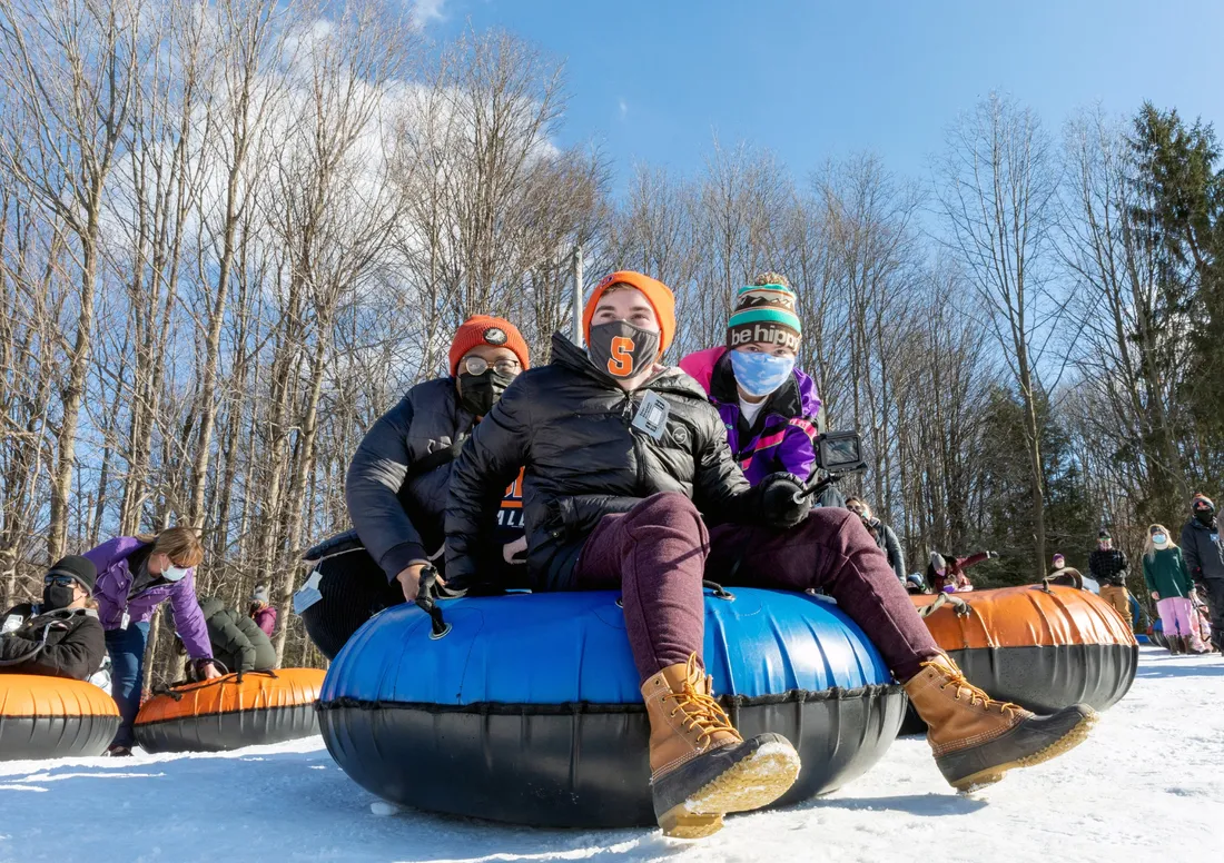 Three people sitting on a snow tube.