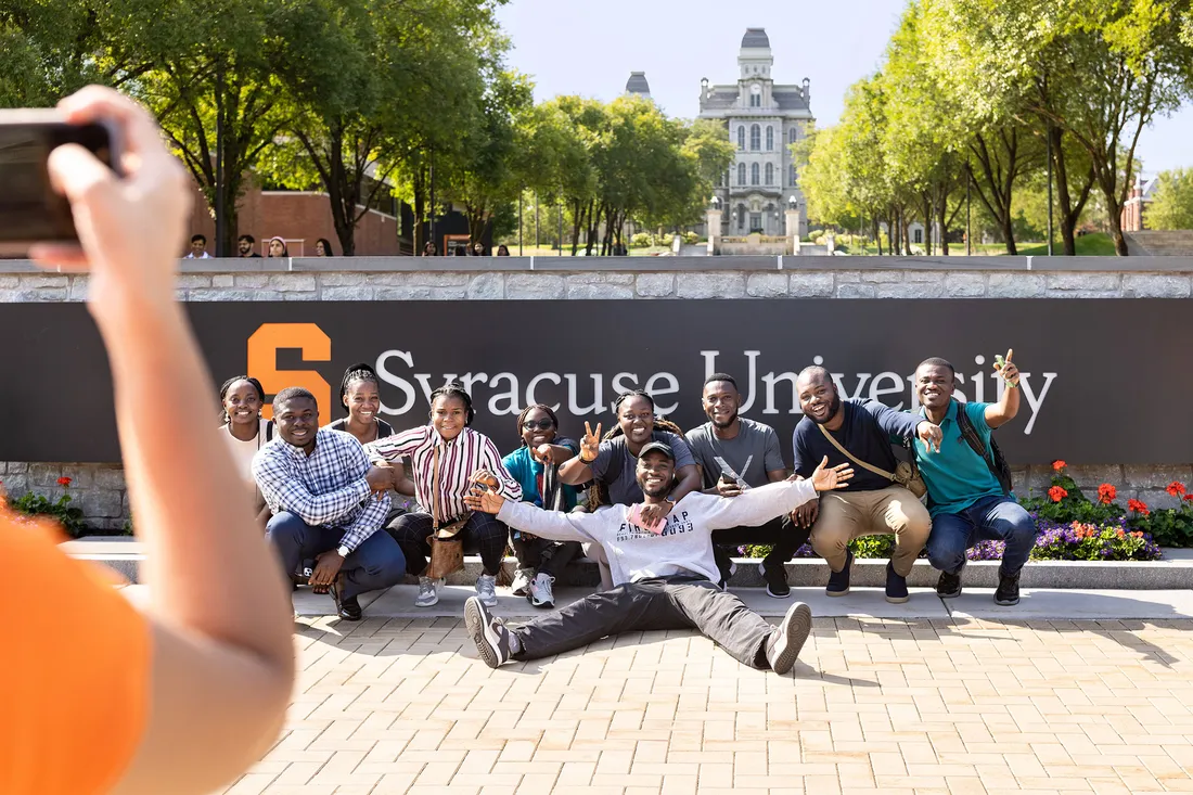 International students standing in front of the Syracuse University sign outside.