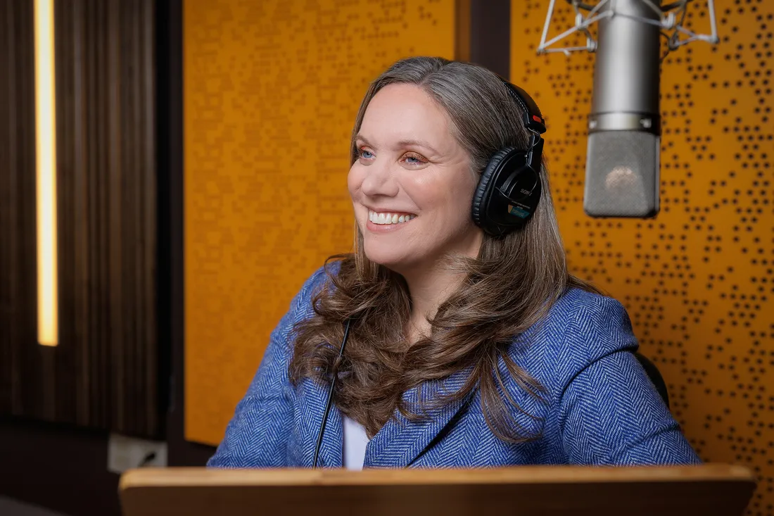 Alumna Diana Dapito ’03 sitting and smiling with a headset on in front of a microphone.