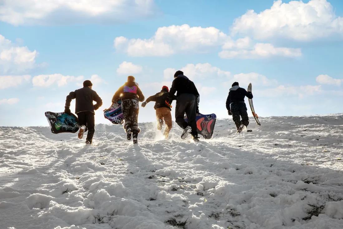 Students running up a hill to go sledding during the winter.