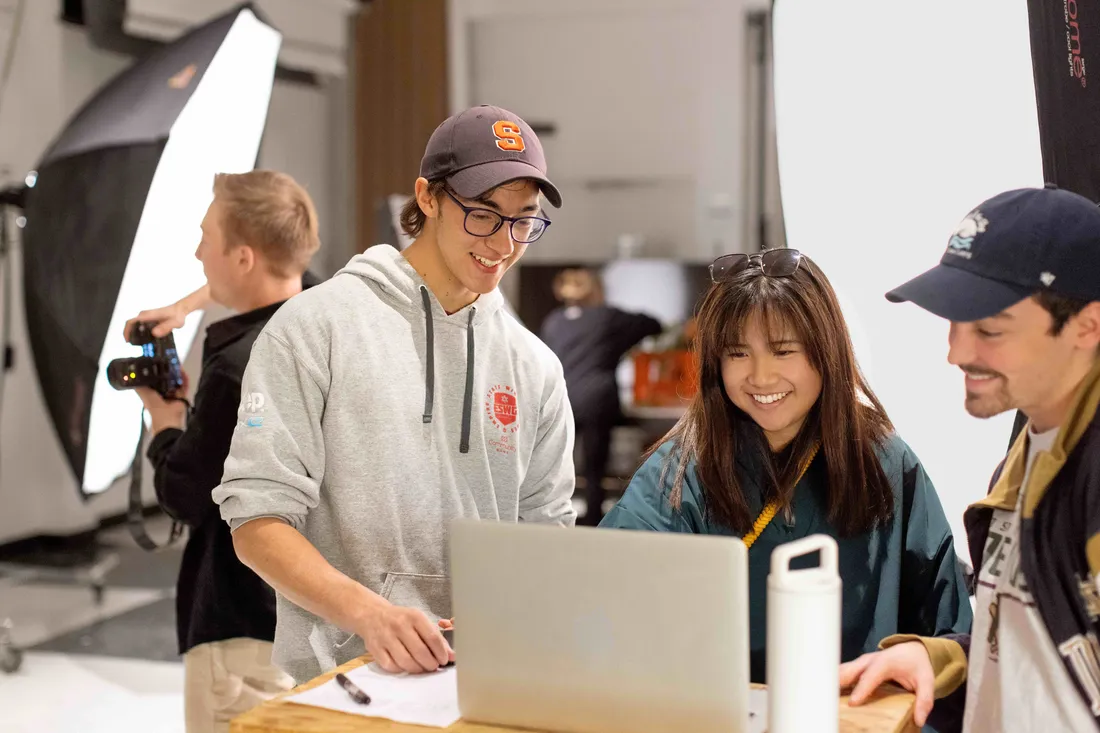 Students smiling and looking at a computer in class.