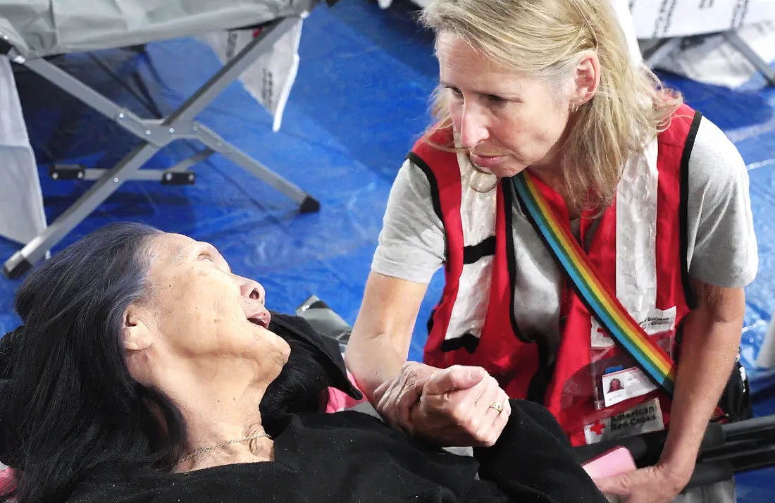 Mimi Teller sitting with someone on a cot.