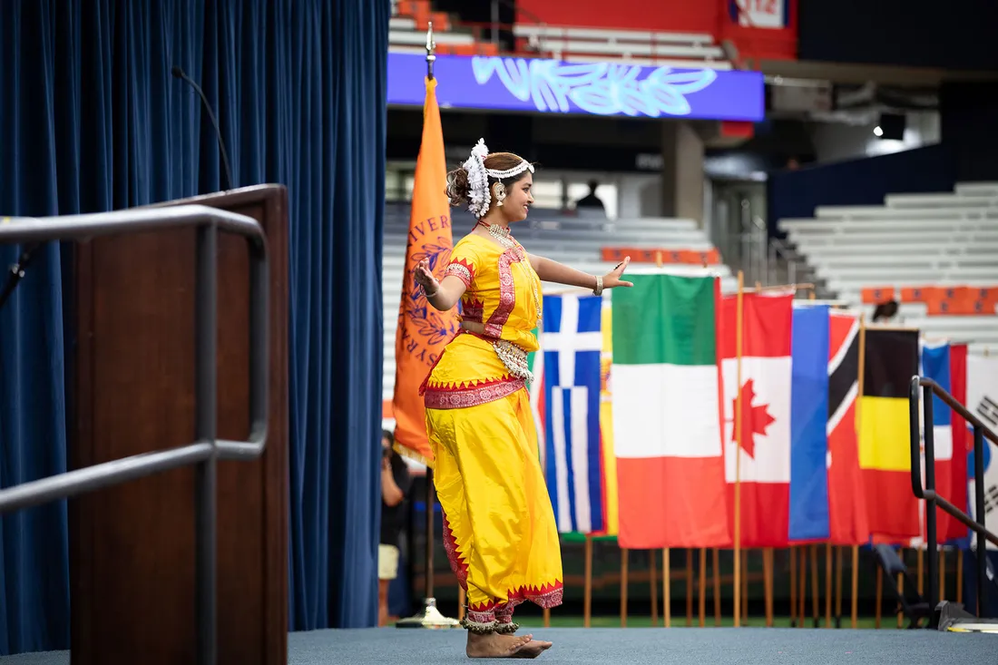Student dances on stage in front of international flags.