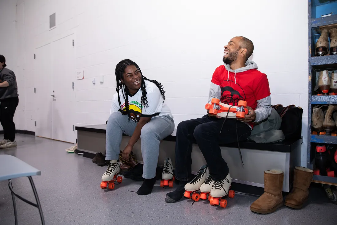 People sitting on a bench and laughing with roller skates on.